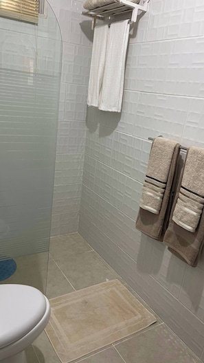 Un baño con inodoro, ducha y dos toallas en un perchero.