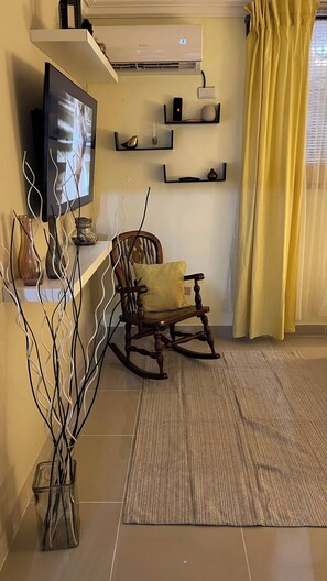 A living room with a television, a rocking chair, a patterned rug, and decorative items on shelves. - Charming First Floor Apartment in Santo Domingo Este (Santo Domingo Este)