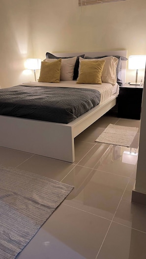 A modern hotel room with a large bed, two bedside tables, and a small rug. - Charming First Floor Apartment in Santo Domingo Este (Santo Domingo Este)