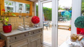 A conservatory with a glass door leading to an outdoor patio area. Inside, there is a wooden cabinet with glassware and a potted plant.