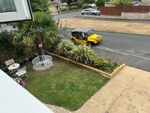 A residential area with a lawn, a small garden bed, and a parked yellow vehicle. - House Sleeps 6 With Enclosed Garden (Cirencester)