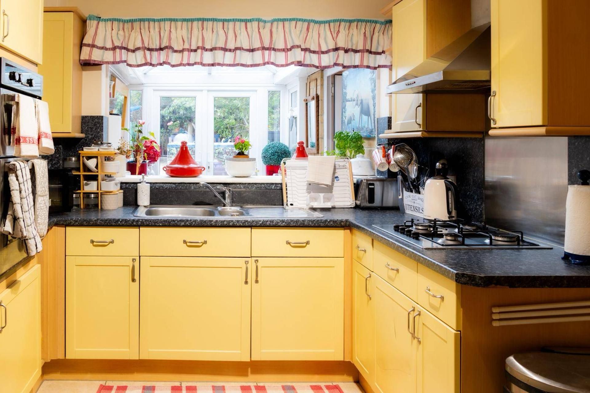 A kitchen with yellow cabinets, a gas stove, a sink, and various kitchen utensils.