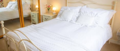 A white four-poster bed with a quilt, bedside tables with lamps, and a mirror.