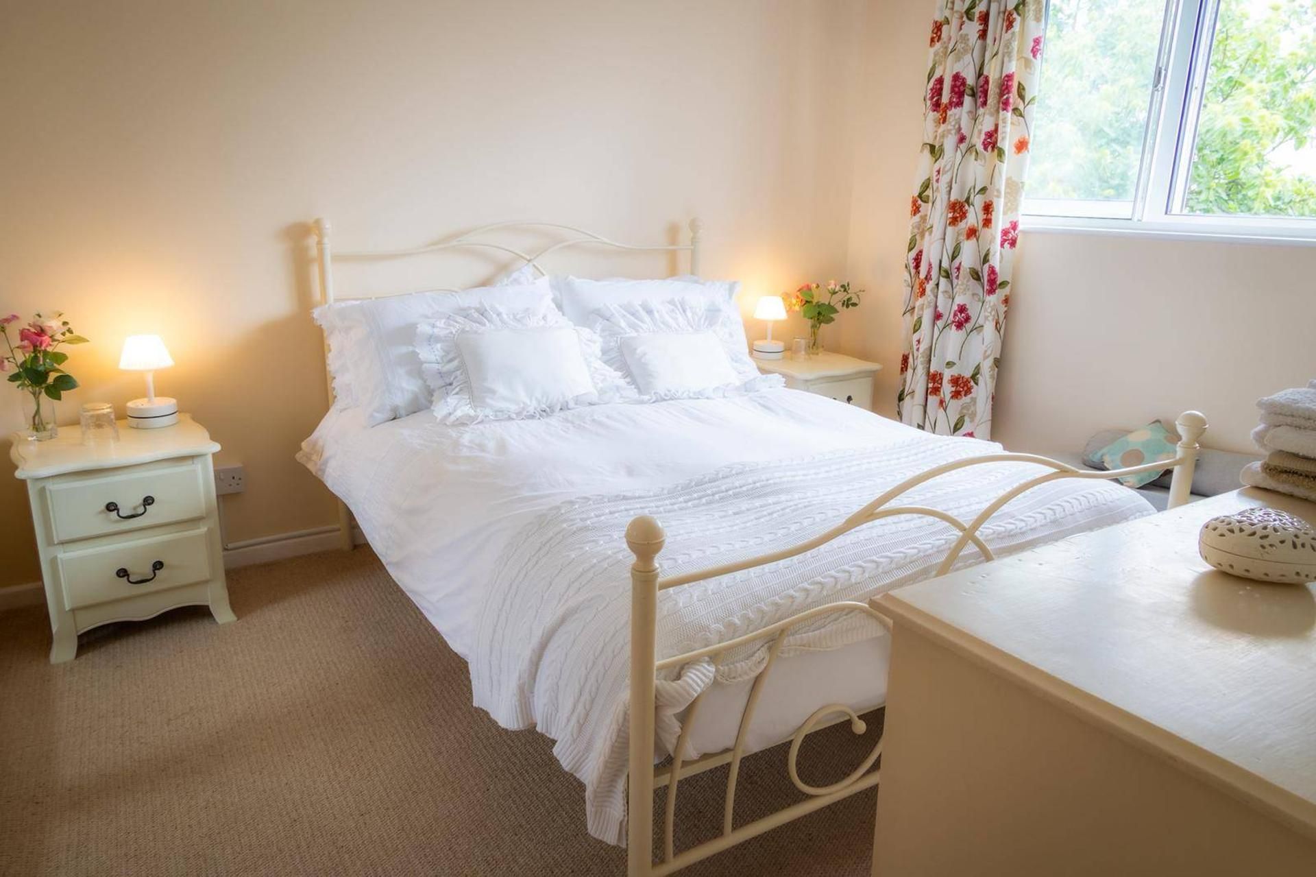 A bedroom with a bed, bedside tables, a lamp, and a window with curtains.