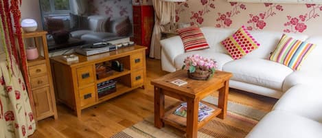 A living room with a television, wooden furniture, a white sofa, and floral wallpaper.