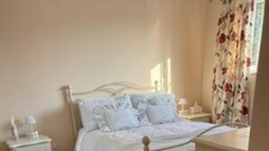 A bedroom with a bed, bedside tables, a chair, and a window with curtains. - House Sleeps 6 With Enclosed Garden (Cirencester)