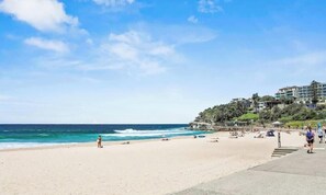 Ein Strand mit klarem Himmel, Meereswellen und einem Gebäude mit mehreren Etagen und Balkonen.