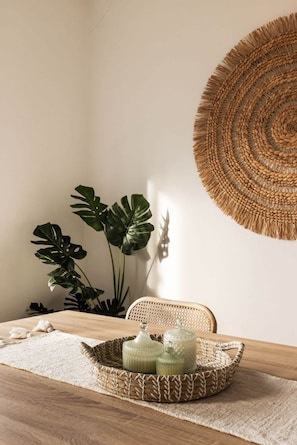 Ein Essbereich mit einem Holztisch, einem gewebten Korb voller Gläser und einem großen Wandteppich.
