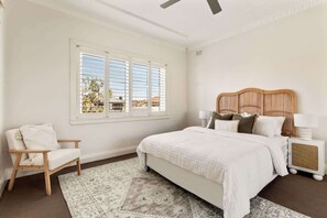 Ein Schlafzimmer mit Bett, Sessel, Nachttisch und Fenster mit Jalousien.