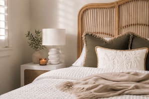 A neatly made bed with a white and beige blanket, a bedside lamp, and a small plant on a bedside table. - The Hideaway | Coastal Escape with Winter Sun & Fine Dining (North Bondi)