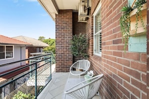 Ein Balkon mit einem weißen Metallstuhl, einem kleinen Tisch und einem Blumentopf.