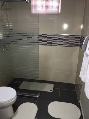 A bathroom with a shower, two toilets, a towel rack, and a window with blinds. - Cozy 2nd Floorapt High Speed Internet (Santo Domingo Este)