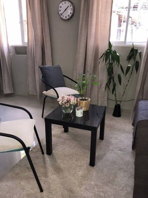 Una habitación con una silla, una mesa, un reloj y una ventana con cortinas.
