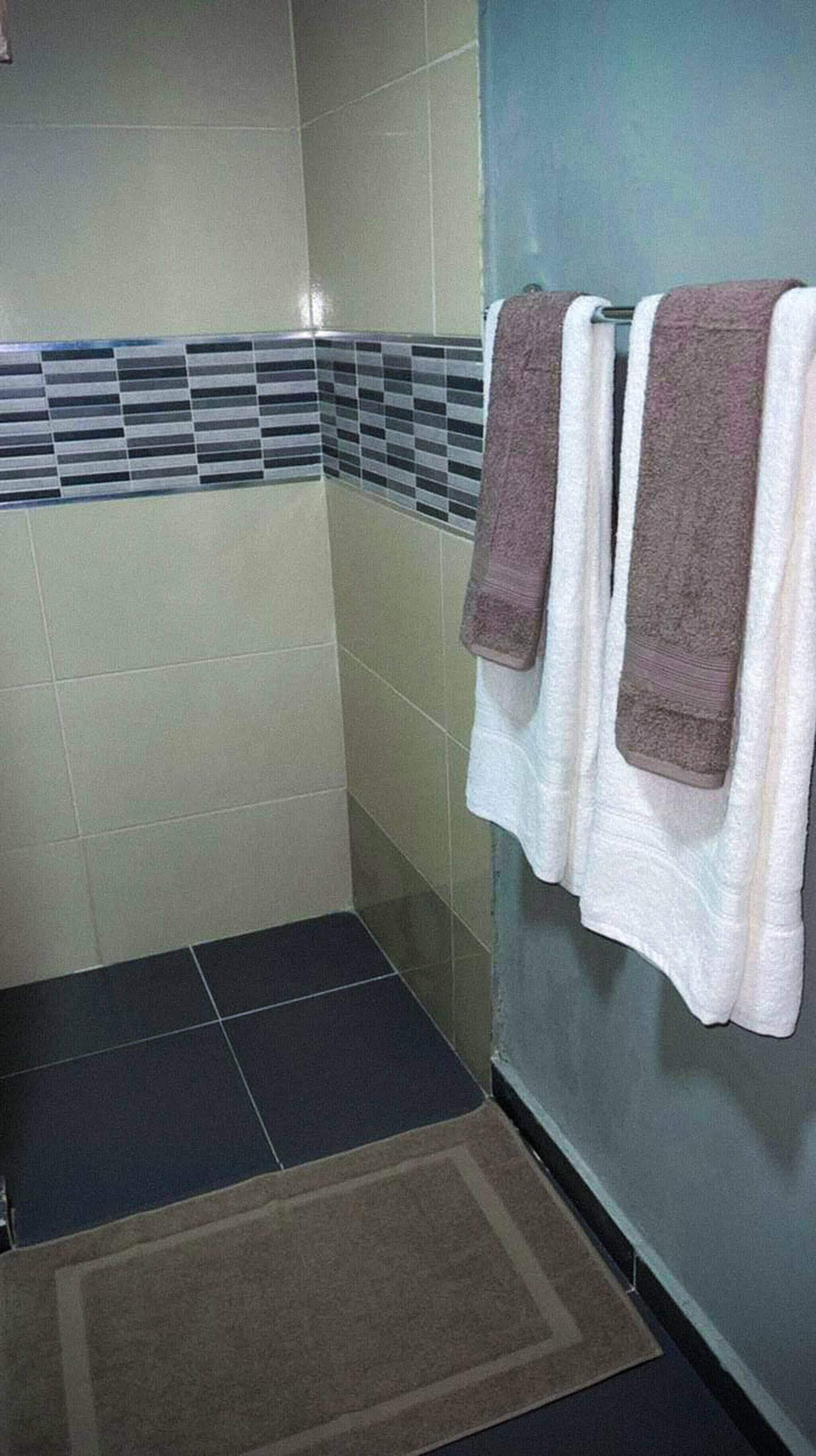 Ein Badezimmer mit gefliesten Wänden, einer Duschkabine und Handtüchern an einem Wäscheständer.