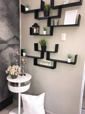 Um banheiro moderno com uma pia branca assentada, um espelho redondo branco e uma prateleira preta fixada na parede, com plantas e uma moldura com uma fotografia.