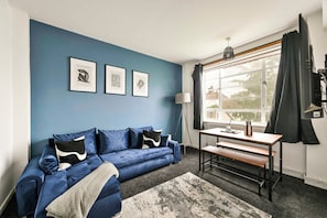 A room with a blue sofa, a wooden table with a bench, and framed artwork on the wall. - Entire apartment in Brixton (London)