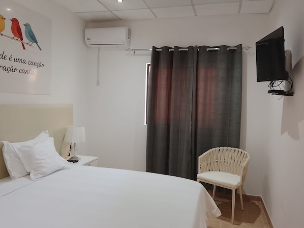 A bedroom with a bed, a chair, a TV, and a window with curtains.