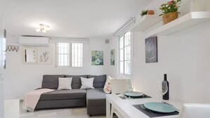 Ein modernes Wohnzimmer mit einem grauen Sofa, einem Esstisch mit einer Weinflasche und einer weißen Wand mit Kunstwerken.