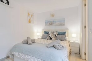 A bedroom with a bed, pillows, a nightstand, a lamp, and a painting on the wall. - Sunny Corner Apt in Puebla Aida Golf (Mijas)