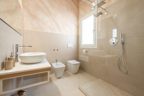 Et moderne badeværelse med stor vask, bidet, toilet og en bruseafdeling med glasvægge.