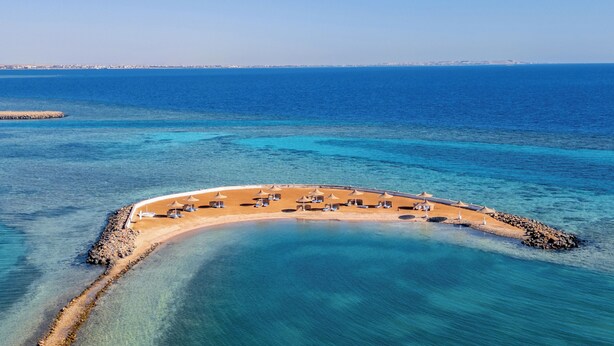 Vista aérea de una playa con aguas azules cristalinas, una costa curvada y una fila de tumbonas.