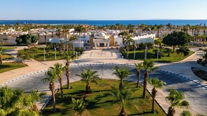 Un resort con un edificio central identificado como 'Coral Beach Resort', rodeado de palmeras y vista al mar.
