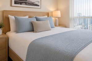 Ein ordentlich bezogenes Bett mit blauer Decke, einem Holzkopfteil und einer Nachttischlampe.