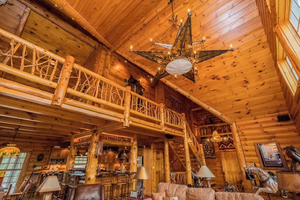 Interior d'una cabana de fusta amb una escala de fusta, una zona de menjador i un gran candelabrum.
