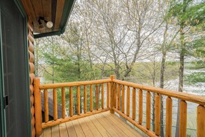 Eine Holzterrasse mit Geländer, die auf einen bewaldeten Bereich mit Bäumen und einem Gewässer blickt.
