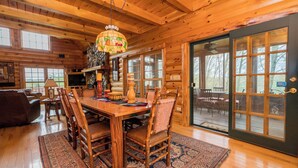 A wooden interior with a dining table, chairs, a chandelier, and a large sliding glass door. - Unique Log Cabin, Hudson Riverfront, minutes to Saratoga (Melrose)