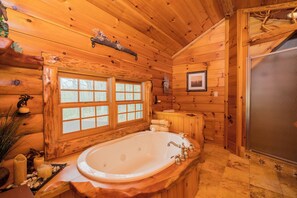 Ein Badezimmer in einer Blockhütte mit einer großen Badewanne, Holzwänden, einem Fenster und einer Duschkabine.