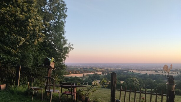 Panorama da un punto elevato su un paesaggio rurale, con una staccionata in legno, sedie e una decorazione a forma di gallo.