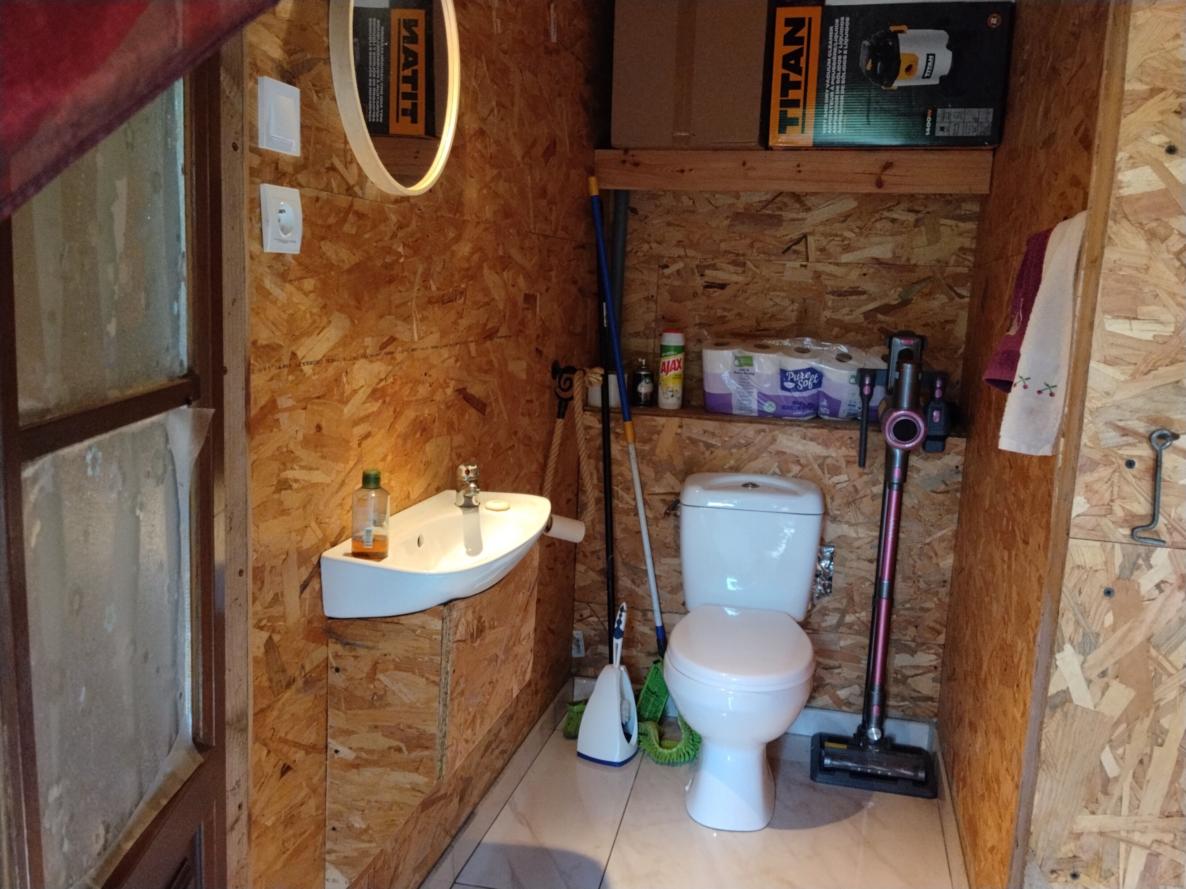Un bagno compatto con lavandino, WC e prodotti per la pulizia.