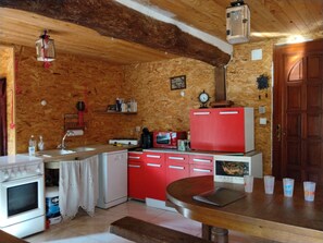 A kitchen with wooden walls, a red refrigerator, a white stove, and a wooden dining table. - La Ferme du Mont Rochard (Sainte-Gemmes-le-Robert)