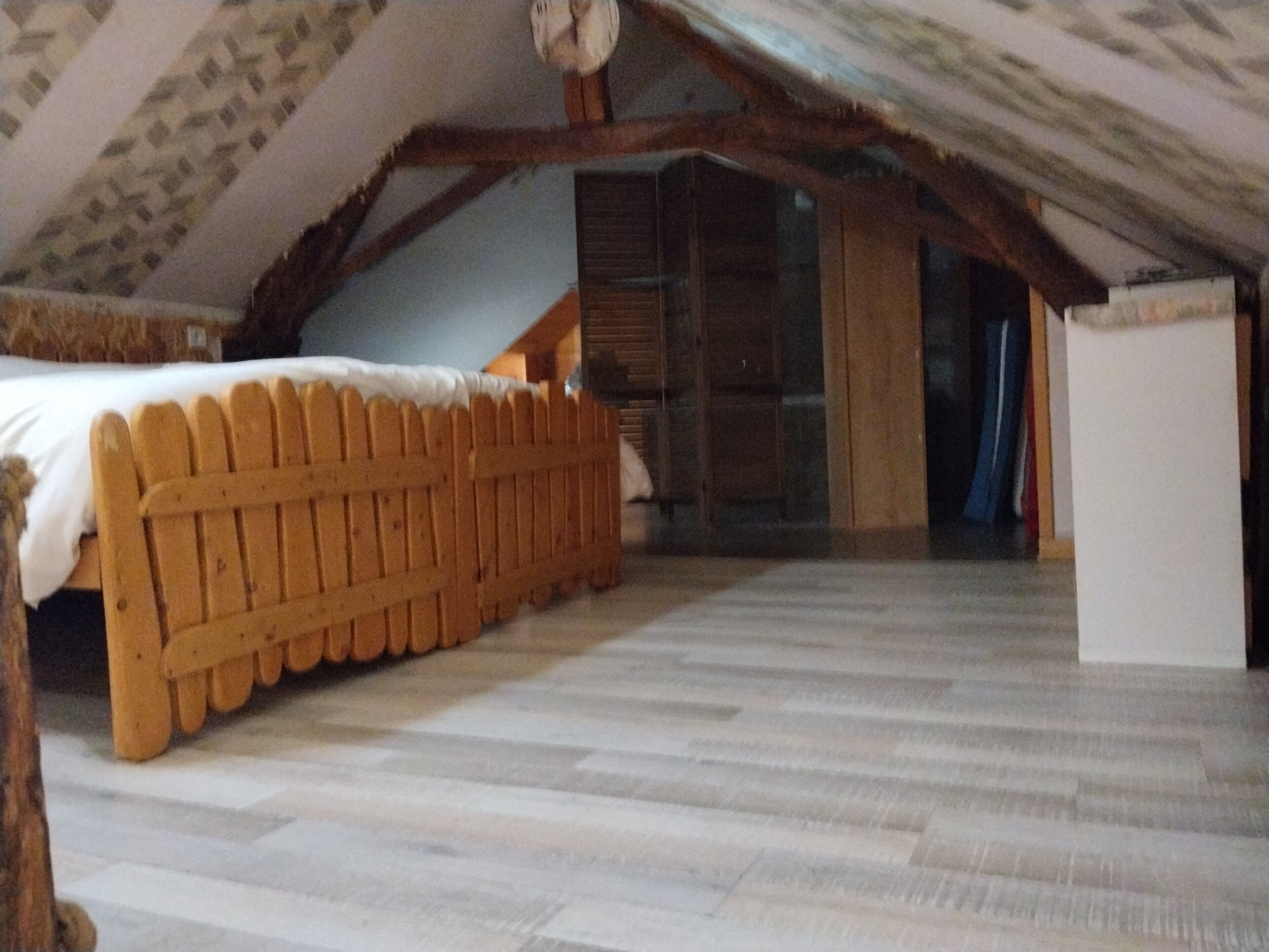 A room with a wooden bed, a small white cabinet, and a sloped ceiling.