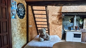 Una stanza accogliente con un letto, una scala in legno, un orsacchiotto, un orologio e un angolo cottura.