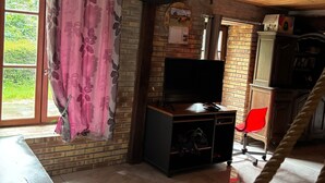 Una stanza con parete in mattoni, soffitto in legno, TV su un mobiletto in legno, una sedia rossa e una scala.