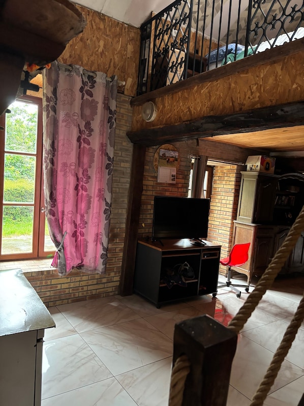 Une pièce avec un mur en briques, un plafond en bois, un téléviseur posé sur un meuble en bois, une chaise rouge et un escalier.