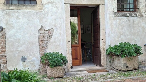 A rustic building with a wooden door, two windows with bars, and a small garden with potted plants. - Artist's Historic Countryside Retreat (Verona)