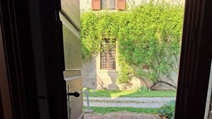 An open door leading to a courtyard with a brick pathway, a doormat, and a building with a window and shutters. - Artist's Historic Countryside Retreat (Verona)