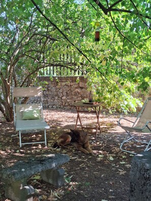 A garden area with a stone wall, a metal chair, a table, and a dog resting on the ground. - Historic Artist's Country House (Verona)
