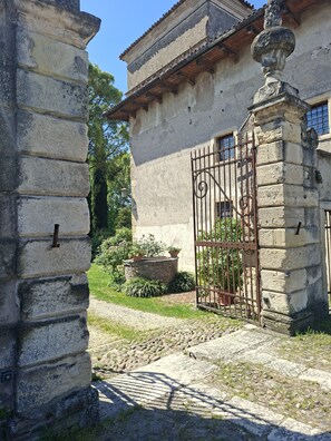 A stone building with a gated entrance, a stone pathway, and a garden with potted plants. - Historic Artist's Country House (Verona)