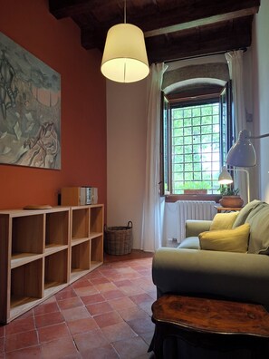 Ein Zimmer mit einer Holzbücherregal, einem Sofa, einer Hängeleuchte, einem Fenster mit Vorhängen und einem Gemälde an der Wand.