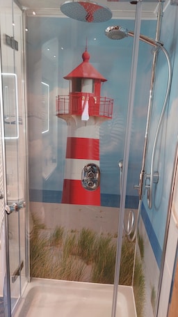 A shower enclosure with a glass door, a red and white lighthouse mural, and a showerhead.. Apartment "Relax in The House By The Forest" with Wi-Fi
