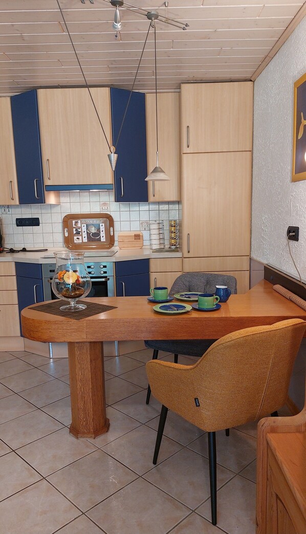 A modern kitchen with wooden cabinets, a dining table, chairs, and a coffee station.