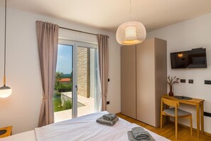A modern bedroom with a bed, a desk, a chair, a TV, and a view through the glass door. - Villa Regina Sea View Retreat near Višnjan (Višnjan)