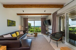 A modern living room with a sofa, coffee table, and a chair, large windows with curtains, and a flat-screen TV. - Villa Regina Sea View Retreat near Višnjan (Višnjan)