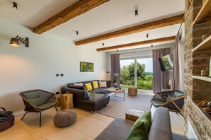 A modern living room with a sofa, chairs, a coffee table, and a large window offering a view of greenery. - Villa Regina Sea View Retreat near Višnjan (Višnjan)