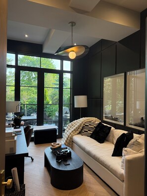 Un salon moderne avec une grande fenêtre, un canapé, une table basse et un bureau avec une lampe.