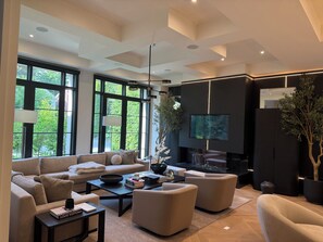 Un salon moderne doté d’un grand téléviseur, de canapés, d’une table basse et d’une grande fenêtre donnant sur un paysage arboré.